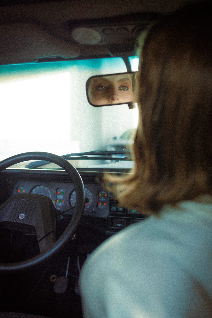 View through a car's rearview mirror of a passenger looking out the window.