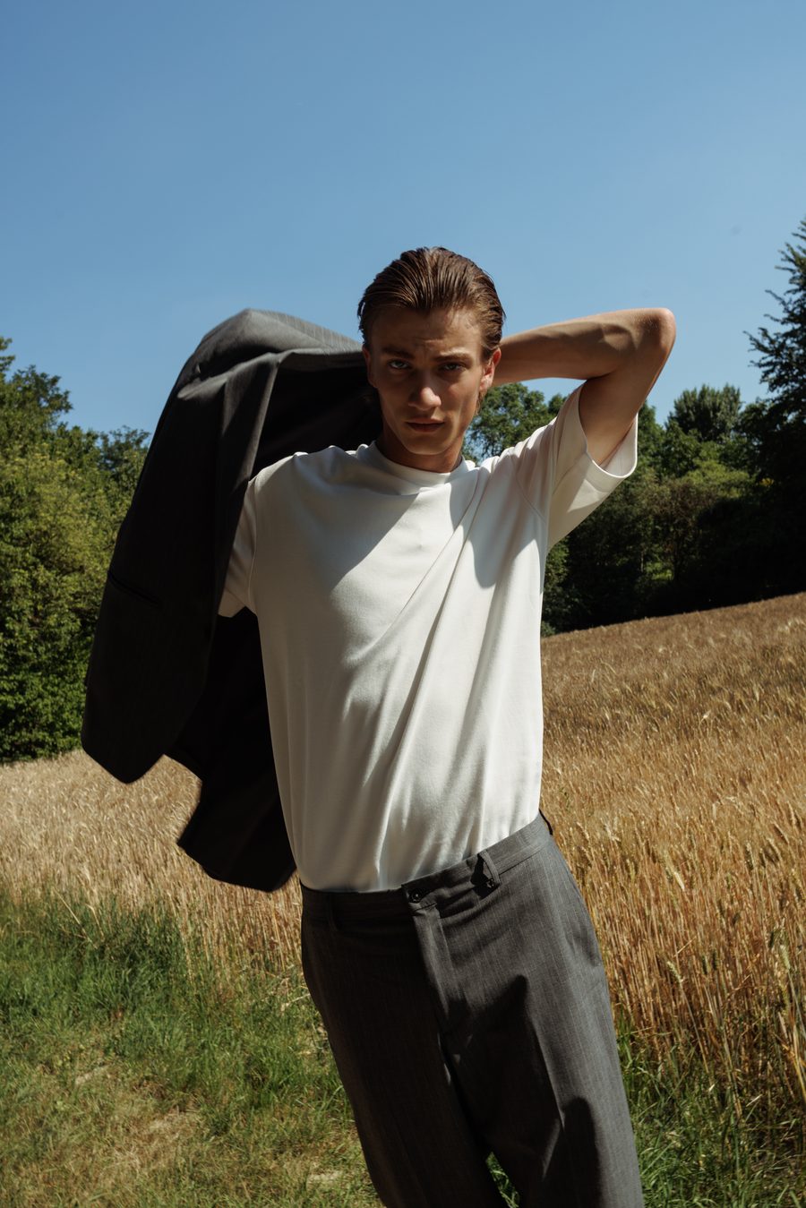 Man in a sunlit field, jacket slung over his shoulder.