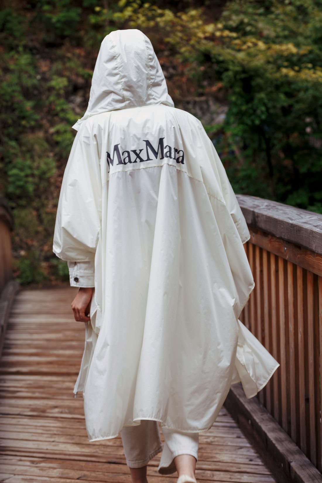 Person in a white MaxMara hooded rain cape walking along a wooden boardwalk, color version.